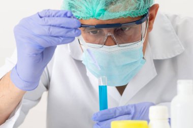 Laboratuvarında test tüplerini doldurmak için boru kullanan genç bir bilim adamının kırpılmış görüntüsü.