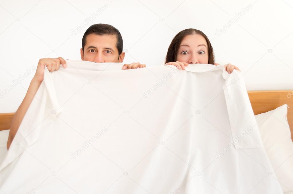 surprised couple is hiding under the sheets