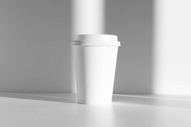 Kapaklı beyaz kahve fincanı, gölge örtüsü, güneş ışığı.