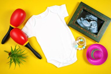 Cinco de Mayo baby romper with sonogram flatlay on a yellow table background clipart