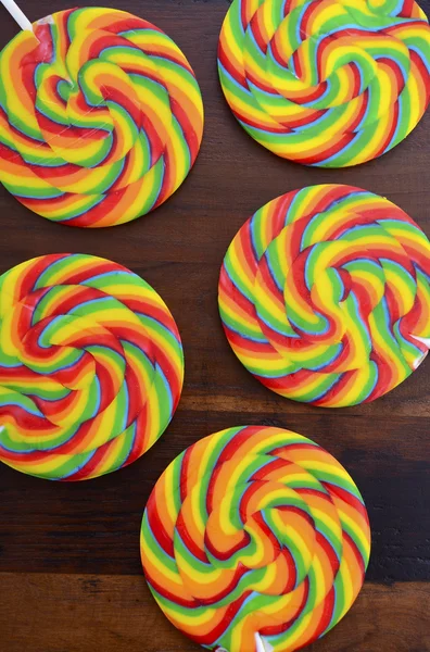 Heldere regenboog lollipop suikergoed op donkere houten tafel. — Stockfoto