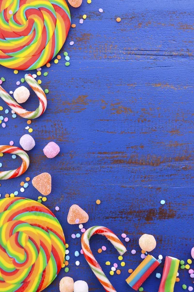 暗蓝色的木桌上明亮的彩虹棒棒糖糖果. — 图库照片