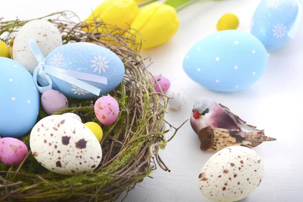 Easter eggs in nest on white wood table. — Stock Photo, Image