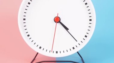 The white clock rotates at a speed for 1 hour from 4:00 AM - 5:00 AM or 4:00 PM - 5:00 PM with a red second hand. The minute and hour hands are black. There are two color backgrounds, blue and pink.