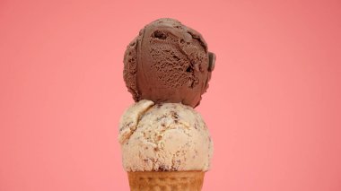 Çikolatalı dondurma, üstünde çikolata parçacıklı külahta, pembe arka planda izole edilmiş.