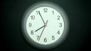 White wall clock tells the time. Rotation of the short and long hands of the clock. On the black background.
