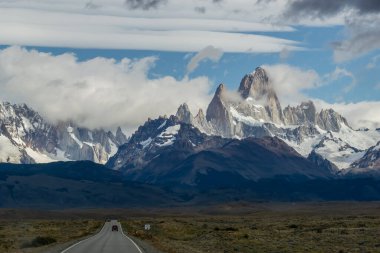 Ufukta kayalık ve karlı bir dağın zirveleri olan ıssız bir yol. Fitz Roy Dağı Arjantin yatay fotoğrafında