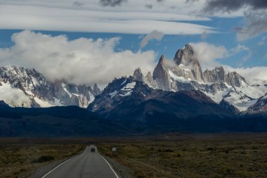 Ufukta kayalık ve karlı bir dağın zirveleri olan ıssız bir yol. Fitz Roy Dağı Arjantin yatay fotoğrafında