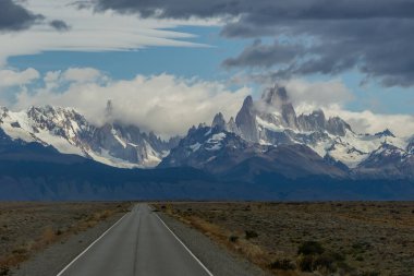 Ufukta kayalık ve karlı bir dağın zirveleri olan ıssız bir yol. Fitz Roy Dağı Arjantin yatay fotoğrafında