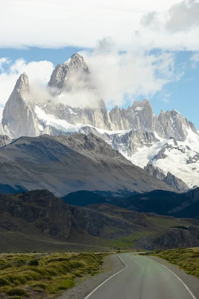 Ufukta kayalık ve karlı bir dağın zirveleri olan ıssız bir yol. Fitz Roy Dağı Arjantin dikey fotoğrafında