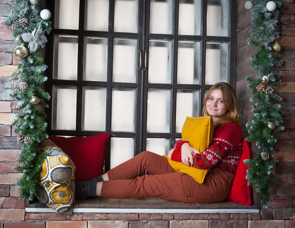 A blonde girl in a red sweater sits on the windowsill. — Stock Photo, Image