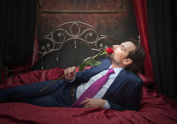 Smiling businessman lying on bed with flower — Stock Photo, Image