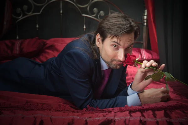 Smiling businessman lying on bed with flower — Stock Photo, Image