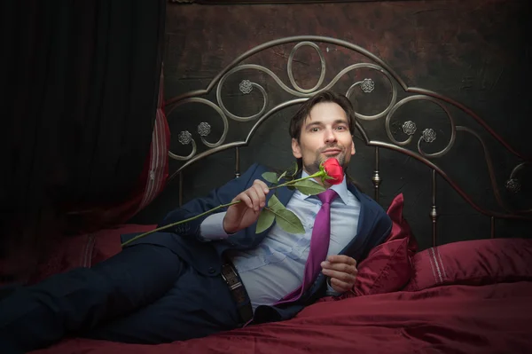 Smiling businessman lying on bed with flower — Stock Photo, Image