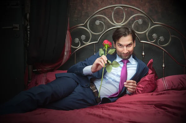 Smiling businessman lying on bed with flower — Stock Photo, Image