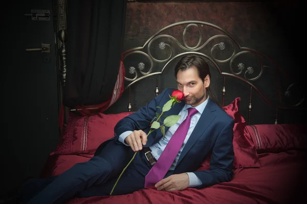 นักธุรกิจที่ยิ้ม นอนบนเตียงพร้อมดอกไม้ — ภาพถ่ายสต็อก