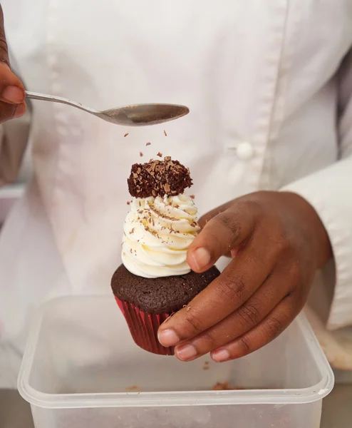 Sprinkles being applied to chocolate cupcake — Stock Photo, Image