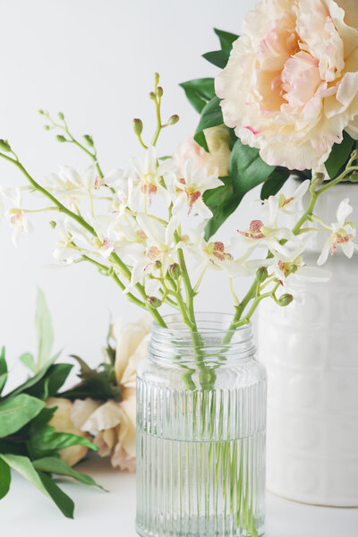 Close up of white orchid flowers in a glass vase with roses in b