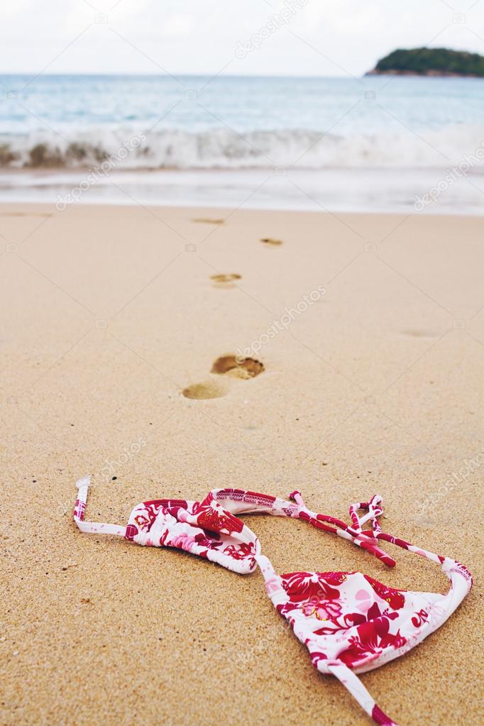 Bikini top lying on beach with footprints into surf