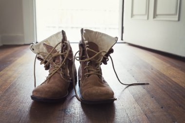 Pair of men's worn leather boots in doorway of home clipart
