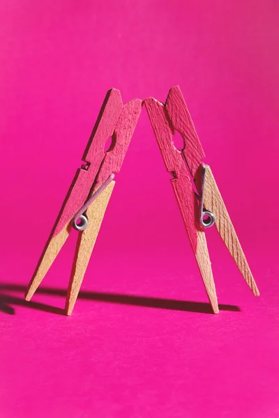 Pair of pink painted pegs symbolising females leaning on each ot Royalty Free Stock Images