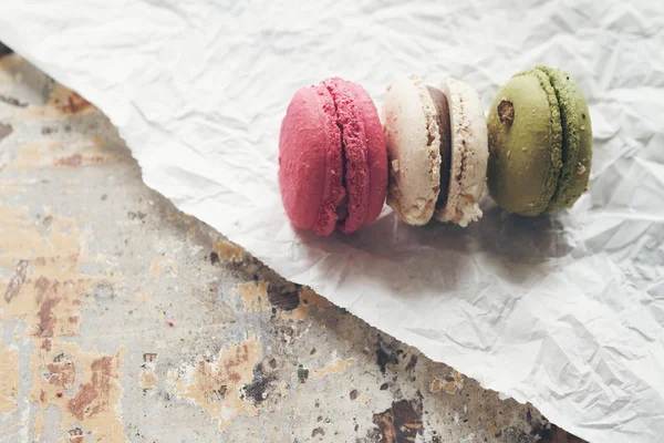 Three macaroon cakes on crumpled paper and rustic table — Stock Photo, Image