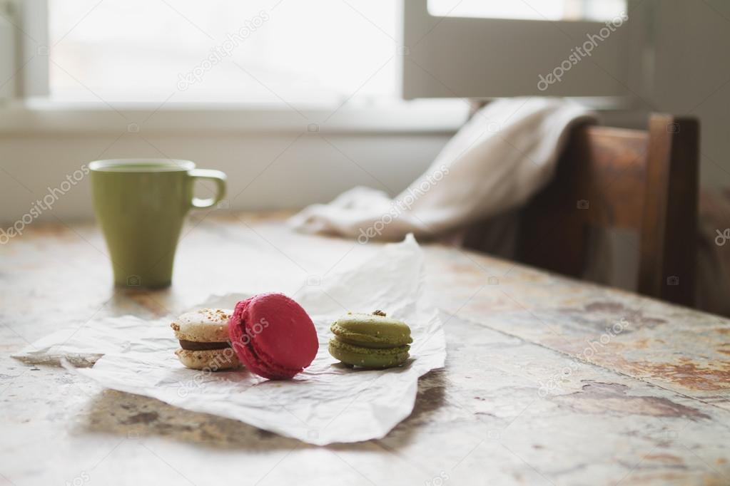 Three macaroons on rustic cafe table with coffee cup