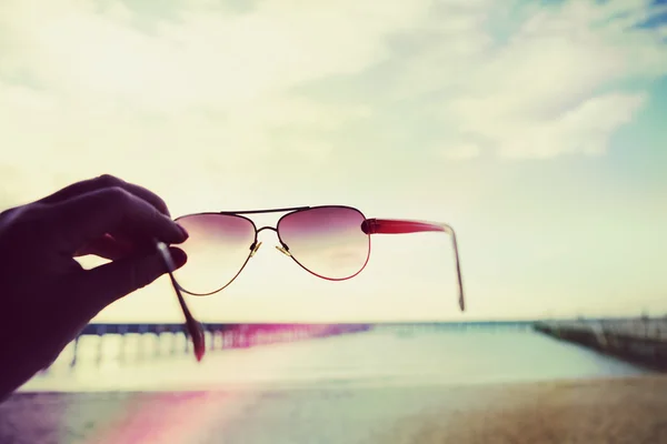 Renkli ışık taraftan holding güneş gözlüğü bir plajda sızdırıyor — Stok fotoğraf