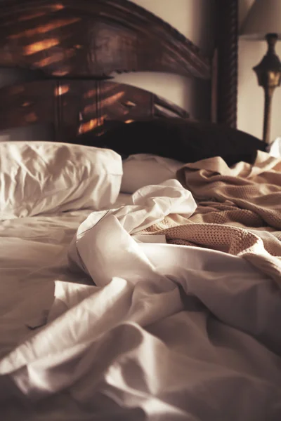 La luz del sol de la mañana en una cama de lujo sin hacer de sábanas blancas y bla — Foto de Stock