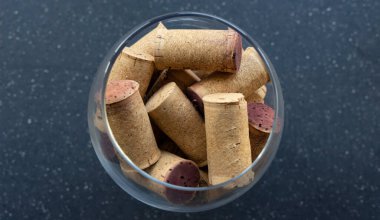 Şarap mantarları şarap kadehinde. Arka planda koyu bir manzara var.