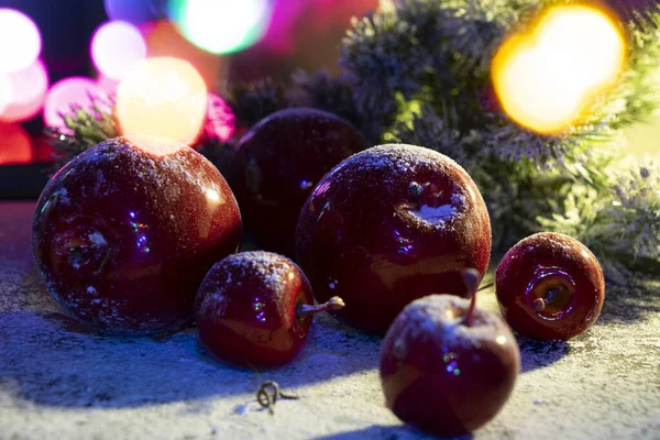 Karda yatan kırmızı elmalar ve yeni yıl ışıklarının ve köknar dallarının arkasına kar serpiştirilmiş.