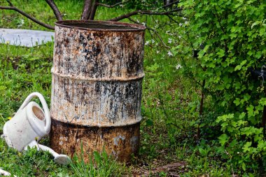 Bahçedeki ağaçların arasında eski bir demir fıçı duruyor.