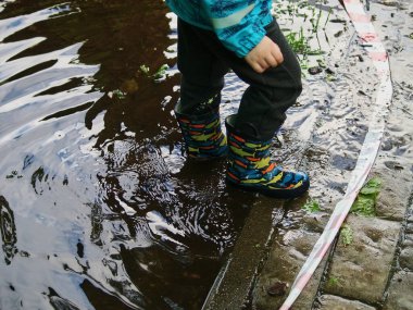 Lastik çizmeli bir çocuk yazın su birikintisinde yürür.