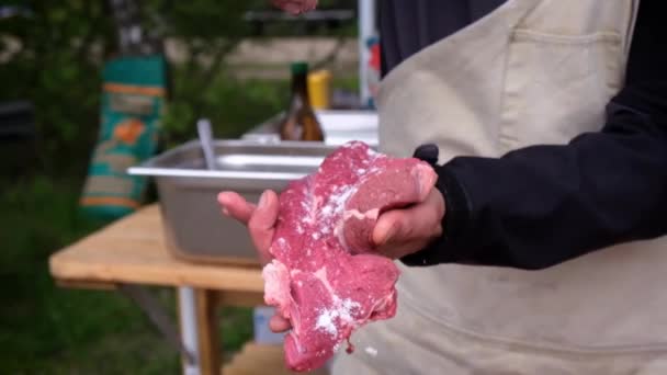 Un trozo de carne fresca es salada por el chef en un delantal — Vídeos de Stock