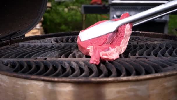 Ein Stück frisches rotes Fleisch wird mit einer Zange auf einen heißen Grill gelegt — Stockvideo