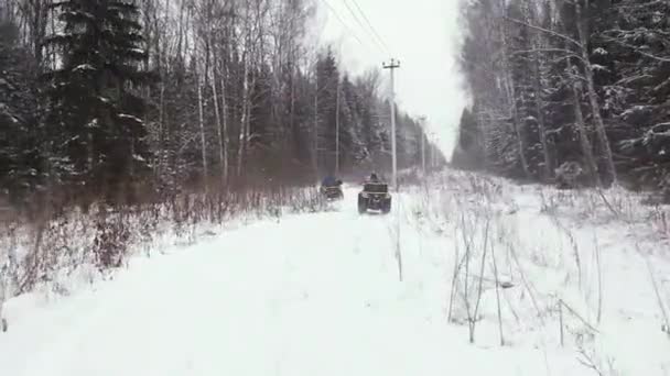 Двое мужчин едут на квадроциклах через зимний лес — стоковое видео