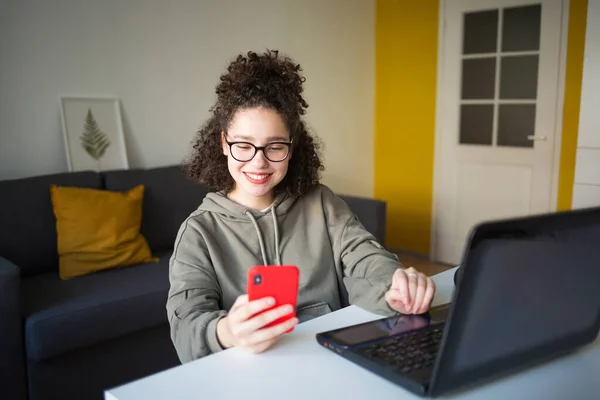 Melez kız bilgisayar ekranında oturup telefona bakıyor. Öğrenciler internet üzerinden konuşuyor. çevrimiçi alışveriş veya evde e-öğrenim.