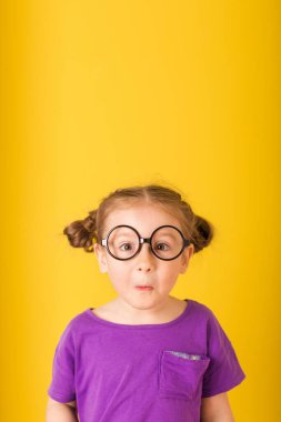 Sarı arka planda mor tişörtlü, sevimli, komik, süpriz çocuk bebek kız çocuğu. çocuk stüdyo resmi