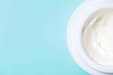 Mavi arka planda fotokopi alanı olan beyaz krema kavanozu. Kozmetik konsepti, cilt bakımı