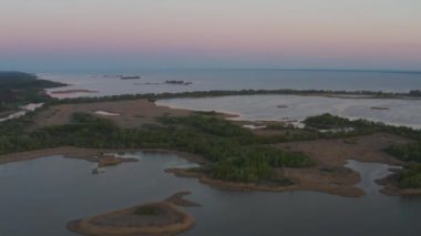Kuru sarı sazlıklar, yeşil ağaçlar, açık mavi gökyüzü, parlak güneş. Birçok martı dalgalar olmadan sakin suyun üzerinde uçar. Nehrin üzerinde akşam batımı. Sudaki ahşap çardak..