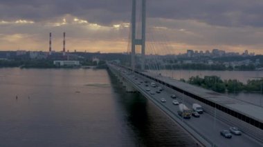Kiev 'deki Dinyeper nehrinin üzerindeki güney köprüsü. Drone film çekiyor. Akşam güneşinin ışınlarında metal telleri olan beton köprü bulutları delip geçiyor. Geniş nehir ve yüksek binalar.