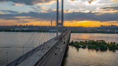 Kiev 'deki güney köprüsü. Dinyeper 'ın üzerinde gün batımı. Akşam şehrinde yoğun bulutlar var. Köprünün akşam çekimi. Gün batımında turuncu güneş. Işınlar bulutları delip geçer ve nehirde yansıtılır..