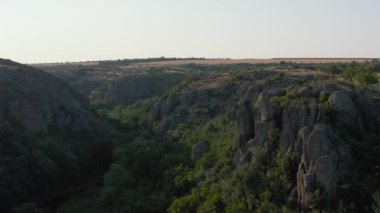 Mertvovod nehrinin Aktovsky kanyonu kuş bakışı. Beyaz taş atan dron, yeşil ağaçlar, bulutlu mavi gökyüzü, kanyonun dibinde sığ bir nehir akıyor. Etrafında sarı kurumuş bir çayır var..