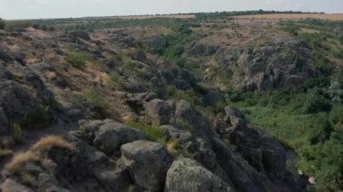 Mertvovod nehrinin Aktovsky kanyonu kuş bakışı. Beyaz taş atan dron, yeşil ağaçlar, bulutlu mavi gökyüzü, kanyonun dibinde sığ bir nehir akıyor. Etrafında sarı kurumuş bir çayır var..