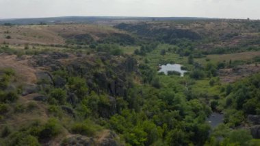 Mertvovod nehrinin Aktovsky kanyonu kuş bakışı. Beyaz taş atan dron, yeşil ağaçlar, bulutlu mavi gökyüzü, kanyonun dibinde sığ bir nehir akıyor. Etrafında sarı kurumuş bir çayır var..