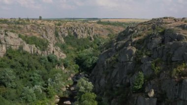 Mertvovod nehrinin Aktovsky kanyonu kuş bakışı. Beyaz taş atan dron, yeşil ağaçlar, bulutlu mavi gökyüzü, kanyonun dibinde sığ bir nehir akıyor. Etrafında sarı kurumuş bir çayır var..