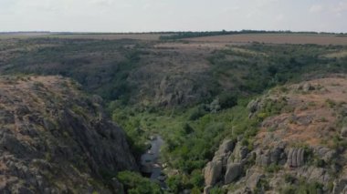 Mertvovod nehrinin Aktovsky kanyonu kuş bakışı. Beyaz taş atan dron, yeşil ağaçlar, bulutlu mavi gökyüzü, kanyonun dibinde sığ bir nehir akıyor. Etrafında sarı kurumuş bir çayır var..