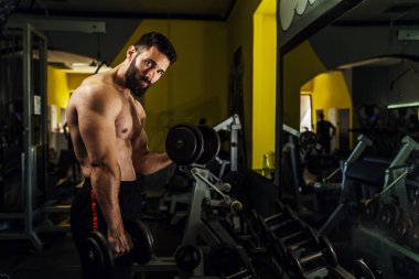 Koyu renk jimnastik salonunda kaslı adam dayanıklılığı üzerine yan görüş sakal kası egzersizi yapan beyaz erkek sporcu halterli pazı - fitness ve güç konsepti kopyalama alanı
