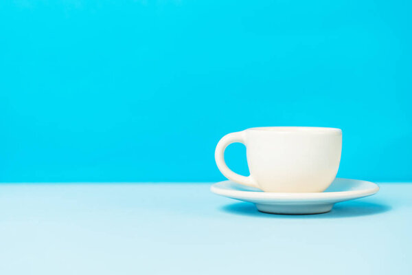 White cup of coffee on the blue background with copy space