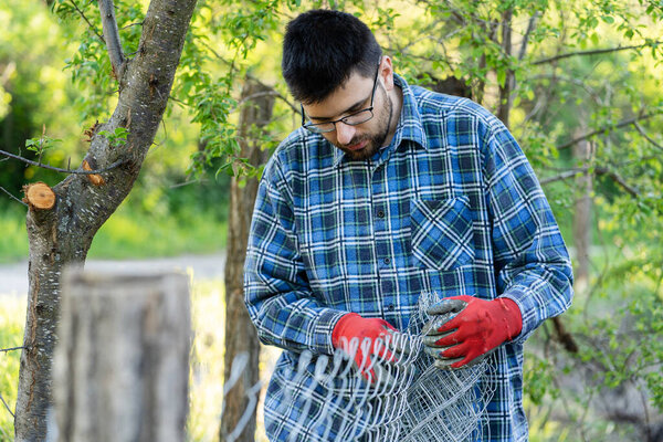 Close up on midsection of young adult caucasian man holding protective chain link diamond wire fence in the field in day with copy space
